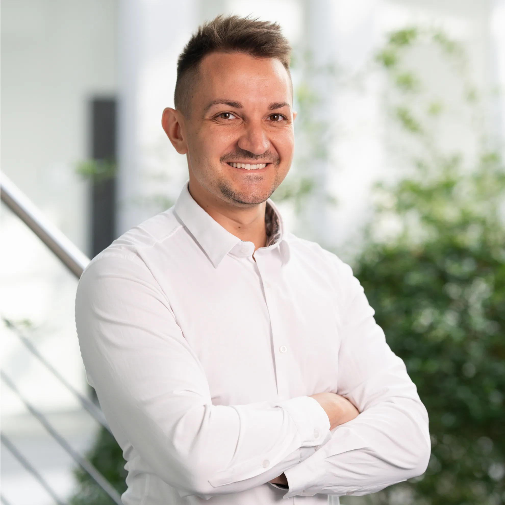 Mitarbeiterportrait - Mann post mit verschränkten Armen lächelnd in die Kamera